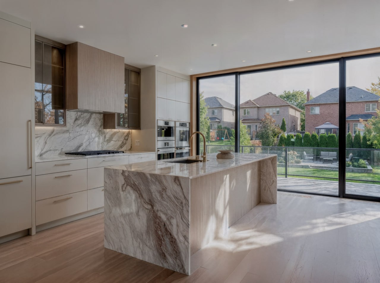 Custom two-tone kitchen with light oak uppers, cream lower cabinetry, and dramatic quartzite waterfall island in a luxury GTA home